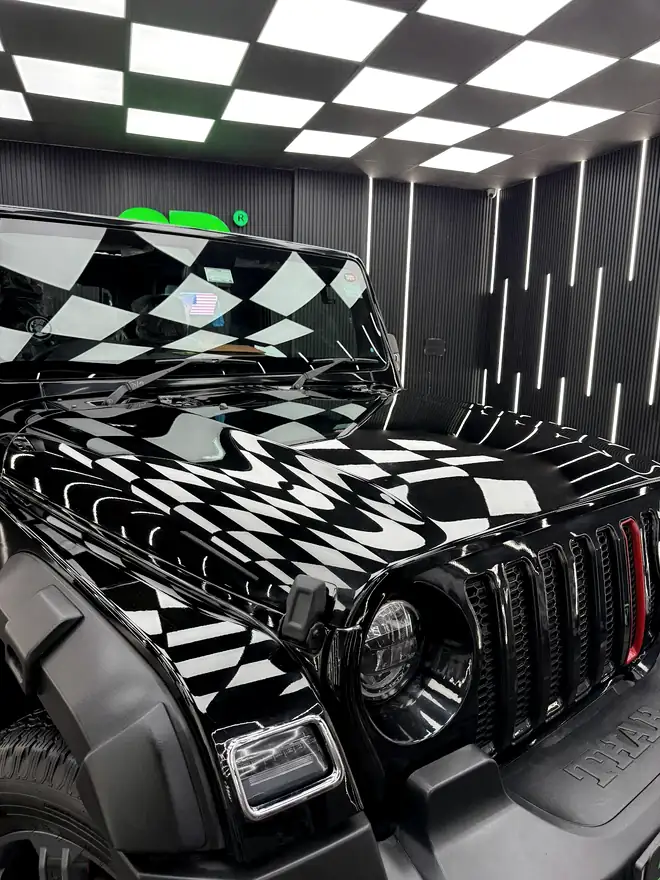 Checkerboard ceiling panels reflected along the bonnet and windscreen of a black vehicle
